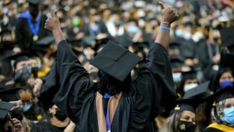 A jubilant graduate celebrating at a commencement ceremony, surrounded by the cheering crowd.