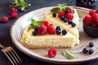 A slice of cheesecake topped with fresh raspberries and blueberries on a plate, symbolizing the poisoned dessert involved in a murder attempt case.