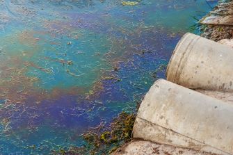 Water contamination at Camp Lejeune, North Carolina, showing pipes discharging polluted water with a rainbow sheen on the surface.