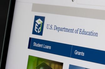 Close-up of a computer screen displaying the U.S. Department of Education site with a logo and navigation tabs labeled 'Student Loans' and 'Grants'.