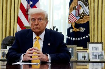 Former President Donald Trump seated at a desk in the Oval Office, with a serious expression.
