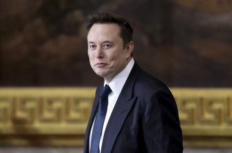 Side-profile portrait of a man in a dark suit and tie in a formal room.