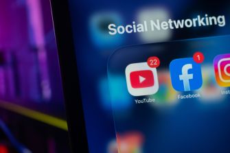 Close-up of a smartphone screen showing social media icons (YouTube, Facebook) and the word "Social Networking."