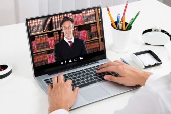 A person using a laptop to video conference with an attorney, surrounded by office supplies and books in the background.