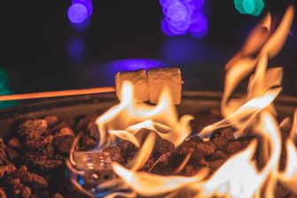 Marshmallows being roasted over an open flame with colorful lights in the background.