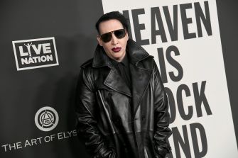 Person wearing a black leather jacket and dark sunglasses standing in front of a backdrop with logos, including Live Nation