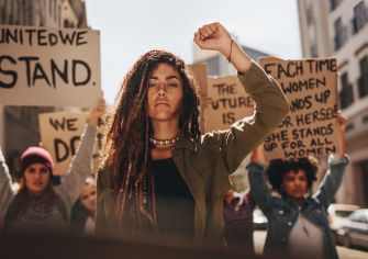 A group of women participating in a protest, holding signs and raising their fists in solidarity.