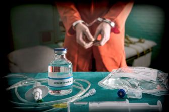 A person in handcuffs with medical equipment and a vial of sodium thiopental on a table.