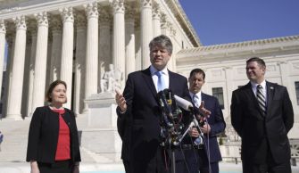 A group of officials speaking at a press conference outside a large government building, addressing issues related to energy policy and public utilities.