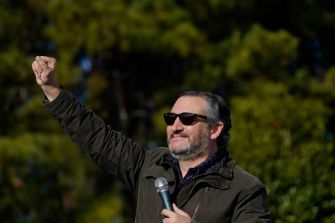 A man raising his fist while holding a microphone outdoors, surrounded by trees.