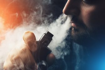 A person exhaling vapor from an e-cigarette in a dark setting.