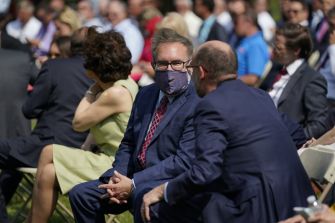 A group of people seated outdoors, engaged in conversation, with some wearing masks.