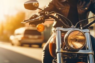 Close-up of a motorcycle with a rider in a leather jacket, highlighting the bike's headlight and signal in a sunlit urban setting.