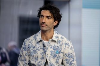 A man with dark hair wearing a floral-patterned jacket, seated in a studio setting.