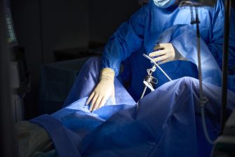Surgeon in blue surgical attire performing a gynecological procedure, with surgical instruments in hand.