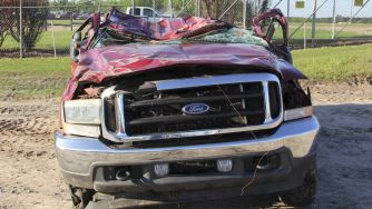 A severely damaged red Ford pickup truck, showing extensive roof collapse and front-end destruction, possibly linked to safety defects in the vehicle's design.