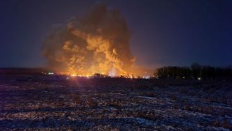 Night view of smoke and flames rising from a train derailment site in Palestine, Ohio, with an illuminated landscape.