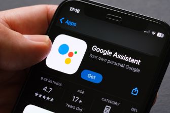 Close-up of a smartphone screen showing the Google Assistant app with the Apps icon and the Google Assistant label, being tapped by a finger.