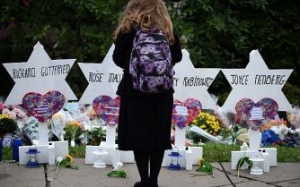 A person stands in front of memorial stars honoring the victims of the Tree of Life synagogue shooting, surrounded by flowers and candles.