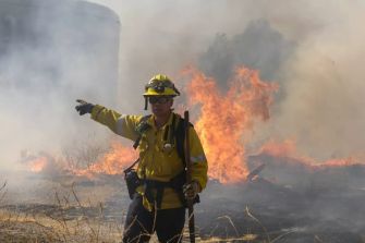 A firefighter directing efforts to control a wildfire with flames and smoke in the background.