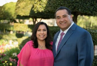 A man and woman pose for a portrait in a garden setting, smiling at the camera.
