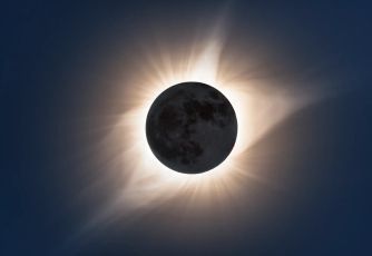 Image of a solar eclipse, showing the moon partially covering the sun with rays of light emanating from around the edges.