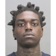 Mugshot of a man with short twisted hair and neck tattoos looking at the camera