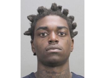 Mugshot of a man with short twisted hair and neck tattoos looking at the camera