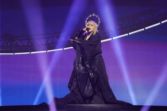 Madonna performing on stage in a dramatic outfit during a concert.