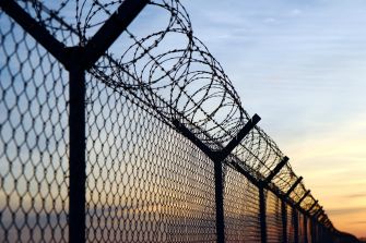 Barbed wire fencing at a prison against a sunset backdrop.
