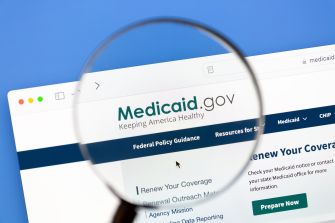 Close-up of a computer screen displaying the Medicaid.gov homepage, viewed through a magnifying glass.