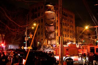 Emergency responders at the scene of a partial building collapse in the Bronx, with visible structural damage and debris.