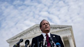 Texas Attorney General Ken Paxton speaks at a podium outside a government building, addressing issues related to abortion laws in Texas.