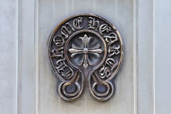 Close-up of a Chrome Hearts metal logo medallion mounted on a light stone wall.