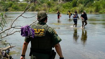 A police officer watches as migrants cross a river near the Texas-Mexico border.