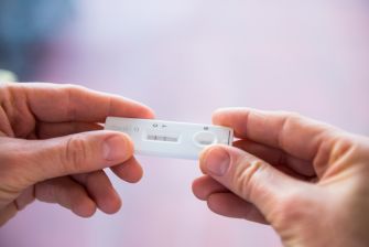 A person holding a COVID-19 test kit, symbolizing the impact of the virus on workplace safety and health.