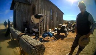 Scene from the film set of "Rust," showing equipment and a character in costume, with a building in the background.