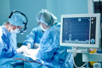Surgical team operating on a patient with a vital signs monitor in the foreground.