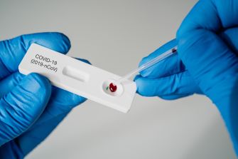 A person in blue gloves using a pipette to apply a sample to a COVID-19 rapid test kit.