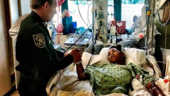 A police officer attending to a shooting survivor in a hospital bed.