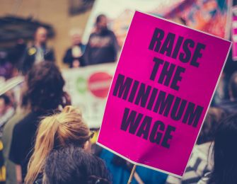 A protester holding a sign that reads "RAISE THE MINIMUM WAGE" during a demonstration.