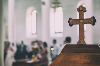 A wooden cross on an altar, with a blurred congregation in a church background.