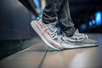 A close-up of a person wearing Yeezy sneakers standing on a tiled floor.