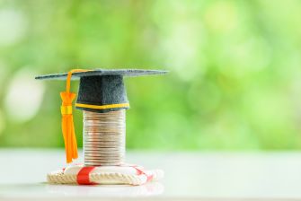 A graduation cap placed on a stack of coins, symbolizing the financial implications of college tuition and the impact of COVID-19 on educational expenses.