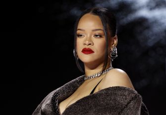 Close-up portrait of a woman with bold red lipstick, dark hair, and large silver hoop earrings against a dark background.