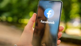 A person holding a smartphone displaying the Facebook logo on the screen.