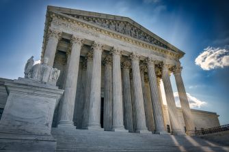 The exterior of the U.S. Supreme Court building, showcasing its iconic columns and architectural details against a clear blue sky.