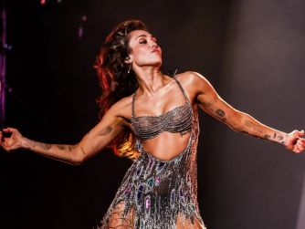 Miley Cyrus performing on stage in a shimmering outfit.