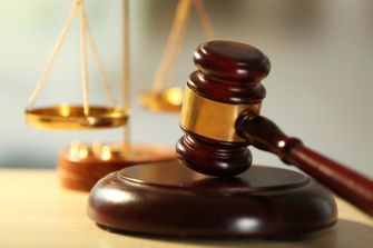 A gavel resting on a wooden block with scales of justice in the background.