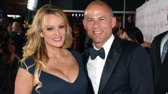 A man and a woman smiling together at an event, with the woman wearing a blue dress and the man in a black tuxedo.